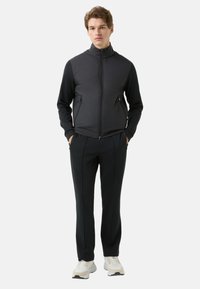 Czarna kurtka na suwak z wysokim kołnierzem, zestawiona z dopasowanymi czarnymi spodniami. Lekka, teksturowana tkanina; białe buty sportowe z akcentami.