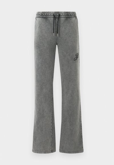 Grijs gewassen brede sweatpants met elastische tailleband en zwarte trekkoorden, met kleine zwarte borduursels op het rechterdijbeen.