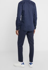 Navy blauwe langemouwen shirt met knopenmanchetten, gecombineerd met bijpassende taps toelopende broek en witte sneakers met blauwe accenten. Glad textuur van de stof.