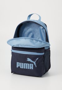 Blå och marinblå ryggsäck med en framficka med dragkedja, prydd med en stor Puma-logotyp, öppen för att avslöja ett tomt inre.