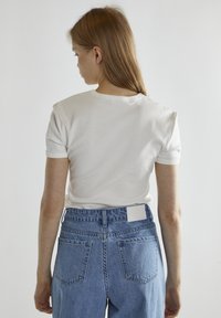 Maglietta bianca a maniche corte con colletto rotondo, abbinata a jeans in denim blu a vita alta con un'etichetta bianca sul retro.