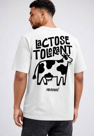 Mann trägt ein weißes T-Shirt mit einer schwarz-weißen Kuhillustration und dem Text „Laktose tolerant“ auf dem Rücken.