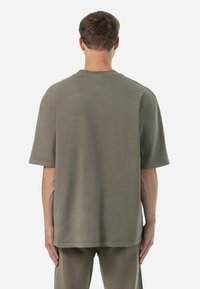 Olive green oversized cotton T-shirt with short sleeves, a crew neck, and a smooth texture. Features minimal stitching and a relaxed fit.