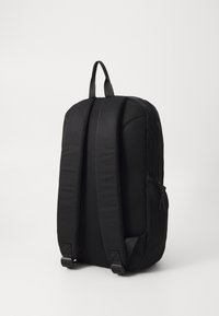 Czarny plecak z wyściełanymi, siateczkowymi paskami, zapinaną na zamek kieszenią boczną oraz eleganckim, opływowym designem. Posiada górny uchwyt do łatwego przenoszenia.