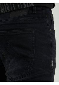 Jeans in denim nero con una finitura testurizzata sottile, tasche posteriori con cuciture decorative e un'etichetta in pelle con il marchio sulla vita.