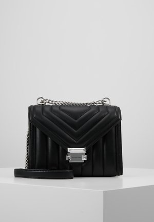 Sac à main en cuir noir matelassé avec une bandoulière en chaîne argentée, présentant un motif chevrons, une base rectangulaire et une fermeture avec un logo en accent.