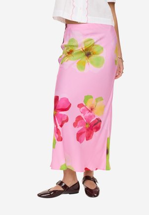 Różowa kwiecista midi spódnica noszona z białym topem i czarnymi lakierowanymi butami Mary Jane, pokazująca boczną stronę i dolną część tułowia osoby.