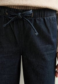 Joggers de mezclilla azul oscuro con cinturilla elástica y cordón ajustable. Textura suave, detalles de costura sutil a lo largo de las costuras.