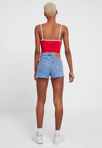 Punainen crop-top valkoisilla hihnoilla, yhdistettynä farkkushortseihin. Shortsit ovat vaaleansiniset, repaleiset, ja niissä on ruskea nahkapatch takana.