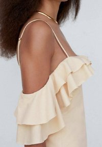 Robe jaune pâle avec des manches épaules dénudées à volants, dotée de fines bretelles et d'un tissu doux et lisse. Vue rapprochée de côté.