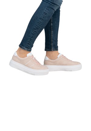 Light pink suede sneakers with a white heel and laces, featuring a thick white sole with ridged texture. Worn with dark blue skinny jeans.