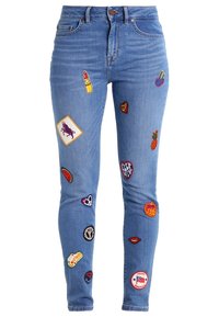 Ljust blå denimjeans med slim fit, som har olika färgglada broderade lappar, inklusive en läppstift, hjärtan och fruktdesigns.