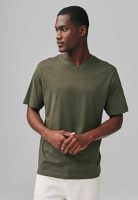 Olivgrön t-shirt med kort ärm och V-halsdesign, slät textur, avslappnad passform och subtila sömsdetaljer, bärs med beige byxor.