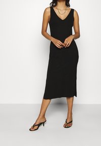 Czarna, żebrowana sukienka midaxi z dekoltem w serek i cienkimi ramiączkami. Pasuje do czarnych sandałów na obcasie z cienkimi paskami. Gładka tekstura, dopasowana sylwetka.
