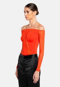 Röd off-shoulder långärmad topp med transparenta paneler och strukturerade sömmar, i kombination med högmidjade svarta satinsbyxor.