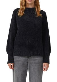 Czarny, prążkowany sweter dzianinowy z długimi, luźnymi rękawami i wysokim kołnierzem. Miękka tekstura i luźny krój, noszony z szarymi dżinsami.