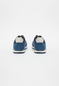 Sapatos de camurça azul-marinho com detalhes azul-escuro e salto cinza-claro, apresentando um design de atacadores e uma superfície texturizada.