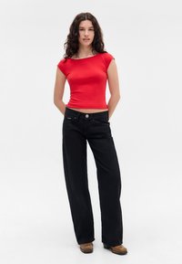 Camiseta roja ajustada con mangas cortas, combinada con pantalones negros holgados con cierre de botón y bolsillos visibles. Textura de tela suave.