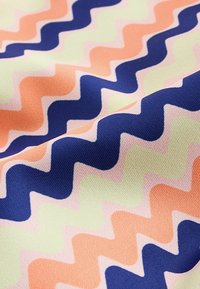 Tissu avec un motif zigzag ondulé dans des couleurs alternées bleu marine, pêche, jaune clair et rose pâle, montrant la texture et les plis.