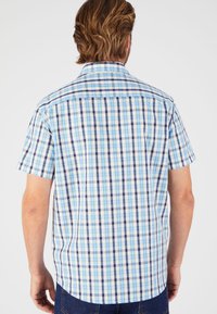Camisa de manga corta, abotonada, con un patrón de cuadros azul y blanco, que presenta diferentes tonalidades de azul y acentos oscuros, fabricada con un tejido ligero.