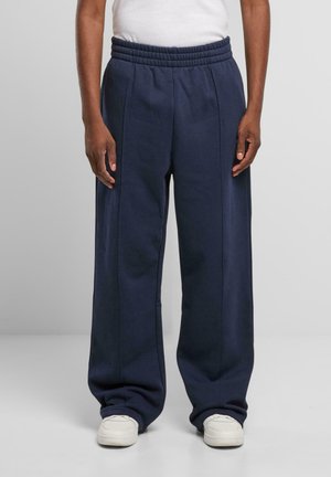 Navy blue sweatpants with a wide-leg design, elastic waistband, and subtle side seams. Made from soft fabric, paired with white shoes.