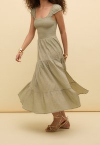 Robe maxi verte à volants, à col carré et manches ruffled ; fabriquée dans un tissu doux et texturé, elle tombe gracieusement jusqu'à l'ourlet.