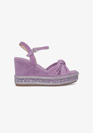 Des sandales compensées en suède violet présentent une bride de cheville, un design à l'avant noué et des détails scintillants embellis autour de la semelle.