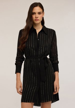 Abito nero con maniche lunghe, presenta motivi a righe verticali e una cintura da annodare. Realizzato in un materiale leggero e trasparente.