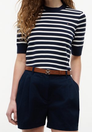 Femme portant un haut à manches courtes rayé bleu marine et blanc, rentré dans un short taille haute bleu marine avec une ceinture marron et une boucle dorée.