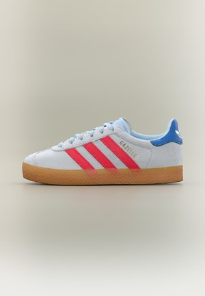 White Adidas Gazelle sneaker with red stripes, blue heel tab, light blue laces, and gum rubber sole on neutral background.