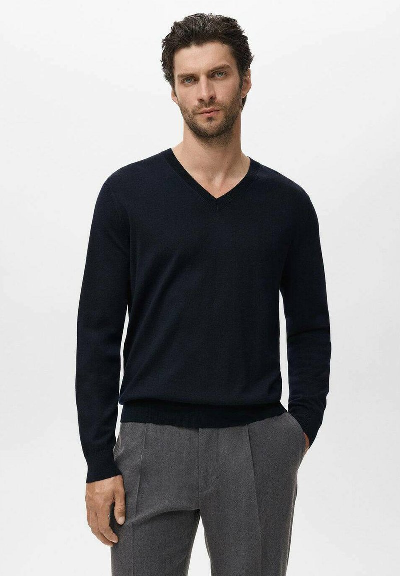 Pull à col en V bleu marine en tricot doux, avec des manches longues et un ourlet côtelé, associé à un pantalon plissé gris.