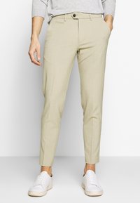 Světlé béžové kalhoty na míru se slim fit, s plochým předním dílem, bočními kapsami a zapínáním na jeden knoflík. Nosené s bílými teniskami.