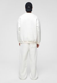 Witte oversized sweatshirt en bijpassende broek van zachte stof. Achteraanzicht toont een ontspannen pasvorm, geribbelde manchetten en een achterzak op de broek.