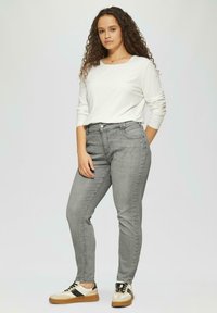 Helle graue Jeans mit schlanker Passform, Fünf-Taschen-Design und subtilen Stitching-Details, kombiniert mit einem weißen Langarmshirt und beigen Sneakers.