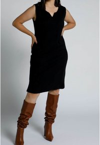 Svart ärmlös klänning med V-ringning, med en figurnära passform. Matcher med bruna knähöga, slappa klackstövlar. Slät textur.