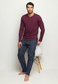 Henley top v hluboké vínové barvě se třemi knoflíky, v kombinaci s námořnickými pruhovanými kalhotami s červenými a bílými pruhy, hladkým materiálem a přiléhavým střihem.
