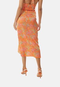 Orange midi dress with a smocked bodice, featuring a colorful dappled pattern in pink and teal, and a flowing, lightweight fabric.