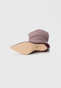 Botte bordeaux à hauteur de genou avec un design ample, un bout pointu, une tige en cuir et une semelle beige lisse avec un petit détail en argent.