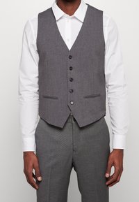 Szary, dopasowany kamizelka o wąskim kroju, z dekoltem w serek, sześcioma guzikami z przodu, dwiema bocznymi kieszeniami oraz gładką teksturą. Połączony z białą koszulą.