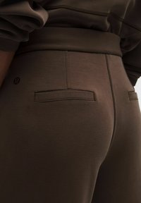 Pantalones deportivos marrones con una textura suave, cinturilla elástica y dos bolsillos traseros. Logo sutil visible sobre el bolsillo derecho.