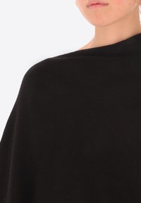 Poncho di lana nera che cade su una spalla, caratterizzato da una texture liscia e un design semplice e minimalista senza motivi visibili.