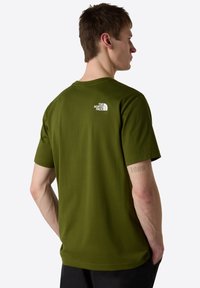 Vihreä puuvillapaita, jossa on lyhyet hihat ja valkoinen logo takana. Pyöreä pääntie ja normaali istuvuus.