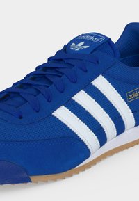 Μπλε αθλητικό παπούτσι Adidas με λευκές ρίγες, μπλε κορδόνια και καουτσούκ σόλα, εμφανίζει το λογότυπο Adidas στη γλώσσα και στο πλάι.