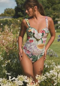 Costume da bagno intero floreale con dettagli verdi, scollo arricciato, motivi di fiori colorati, design aderente e bretelle di media larghezza.