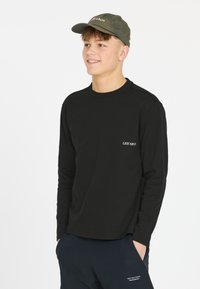 Schwarzes Langarmshirt mit Rundhalsausschnitt und kleinem weißen Logo, kombiniert mit navyblauen Hosen, die ein dezentes Logo-Detail aufweisen.