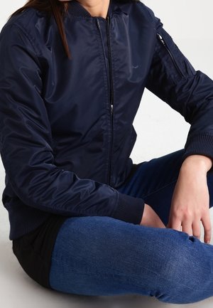 Chaqueta bomber azul marino con cremallera, puños acanalados y un bolsillo en la manga, fabricada con un tejido suave y ligero.