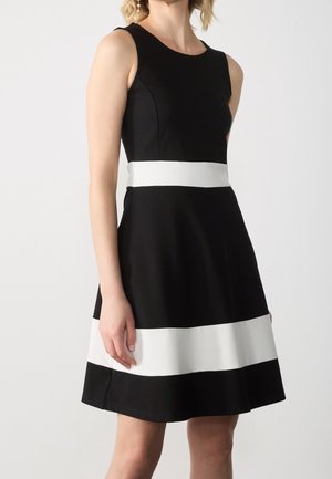 Robe noire sans manches avec une bande horizontale blanche à la taille et une jupe évasée. Tissu doux à la texture lisse.