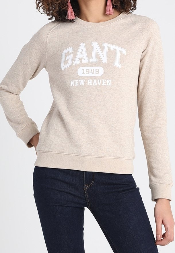 Sudadera beige con cuello redondo, que presenta el texto blanco "GANT 1949 NEW HAVEN" en la parte frontal. La tela tiene una textura suave y puños ajustados.