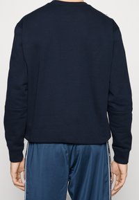 Marine sweatshirt met lange mouwen, ronde hals en textuurstof. Heeft ribgebreide manchetten en zoom, gecombineerd met donkerblauwe sportbroek.
