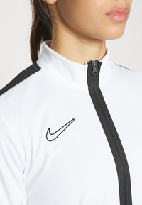 Witte sportieve zip-up jas met zwarte accenten en een klein geborduurd Nike-logo. Textuurstof met een hoge kraagontwerp.